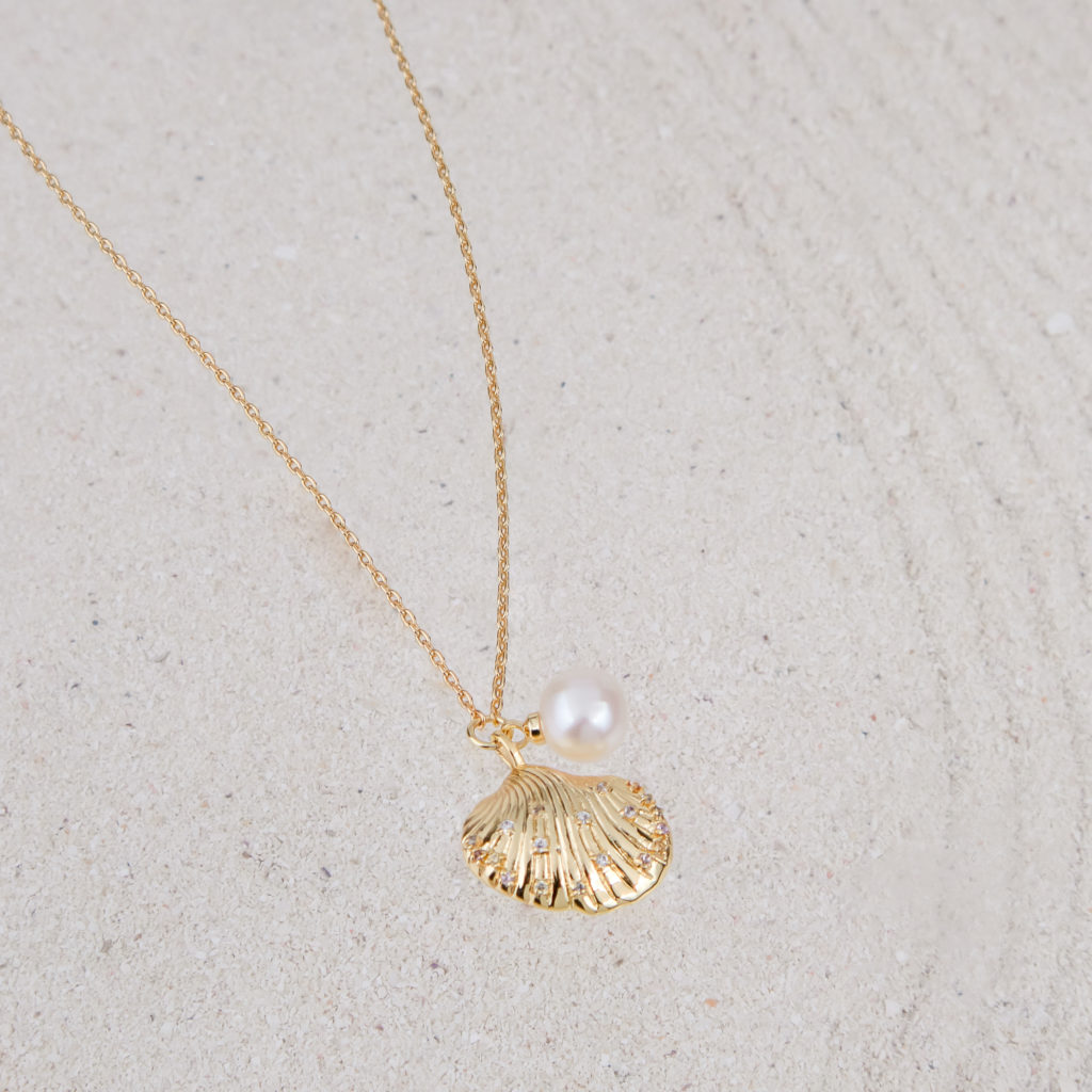 Gold seashell pendant and necklace on white sand
