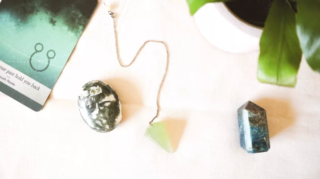 Green crystal pendulum next to two polished crystals.