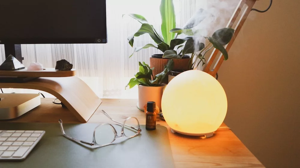 A moon-shaped oil diffuser sitting on desk next to a computer.