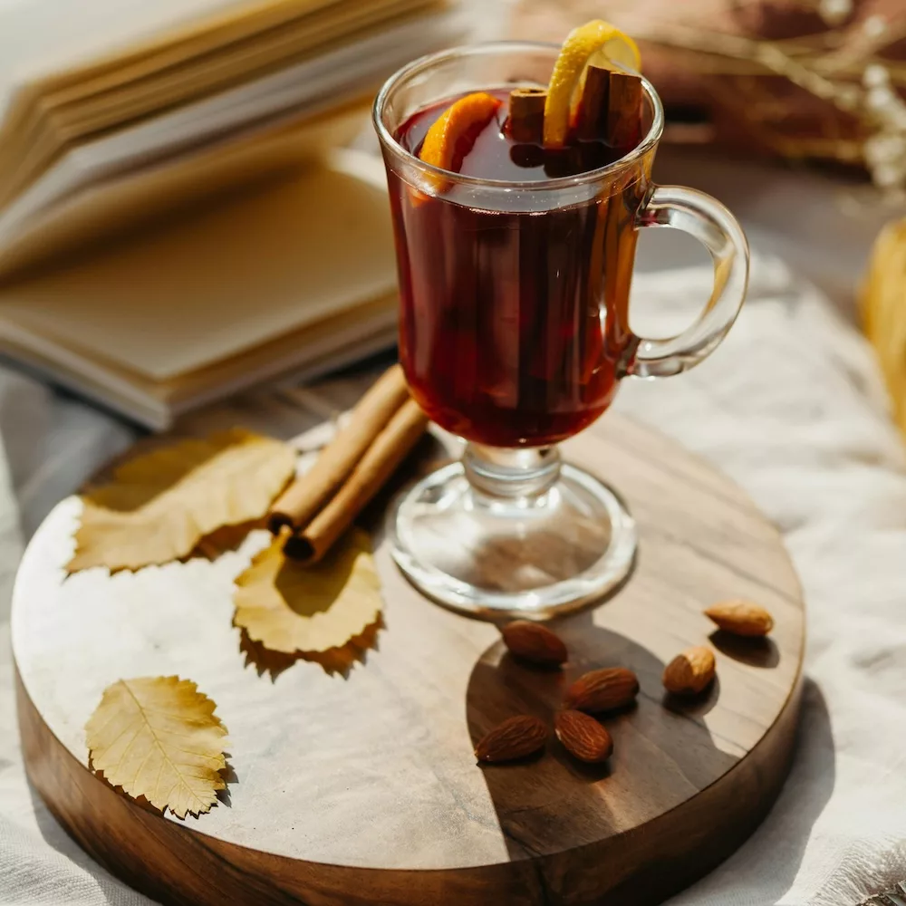 A clear glass of hot tea sitting on a platter with cinnamon and almonds.